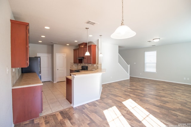 kitchen with pendant lighting, stainless steel refrigerator, light wood-type flooring, and tasteful backsplash