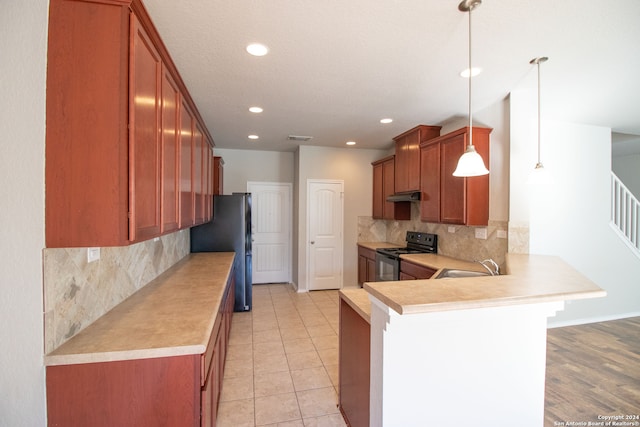 kitchen with black range with electric stovetop, stainless steel fridge, kitchen peninsula, decorative light fixtures, and a breakfast bar