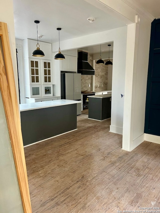 kitchen with wall chimney exhaust hood, hardwood / wood-style flooring, a center island, white fridge, and decorative backsplash