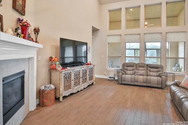 living room featuring wood-type flooring, a high ceiling, and a tiled fireplace