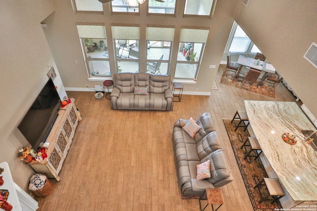 living room with ceiling fan, light hardwood / wood-style floors, and a towering ceiling