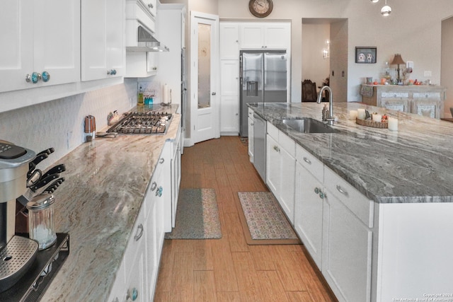 kitchen with appliances with stainless steel finishes, sink, stone counters, white cabinets, and range hood