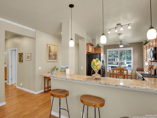 kitchen featuring light hardwood / wood-style floors, light stone counters, kitchen peninsula, stainless steel appliances, and a textured ceiling