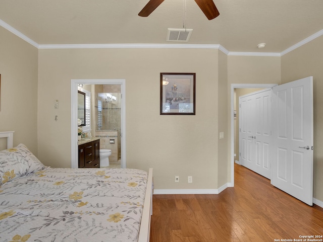 bedroom with a closet, light hardwood / wood-style flooring, ensuite bath, crown molding, and ceiling fan