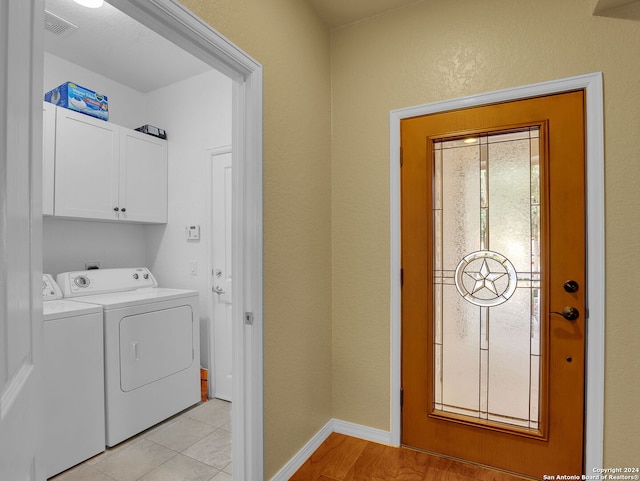 clothes washing area featuring cabinets, light tile patterned floors, and washing machine and clothes dryer