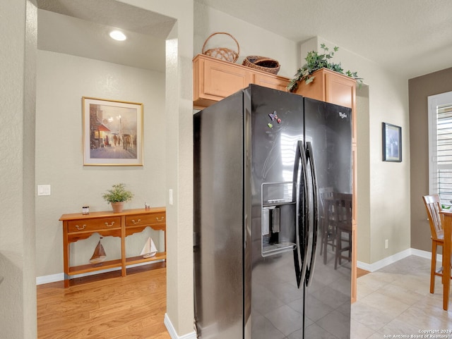 kitchen with light brown cabinets, a textured ceiling, light hardwood / wood-style floors, and black fridge with ice dispenser