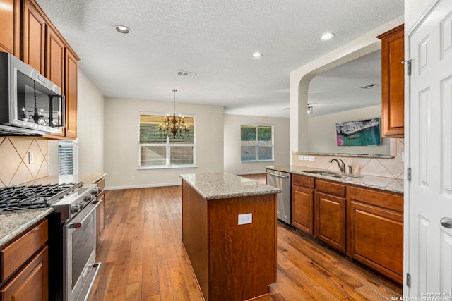 kitchen with stainless steel appliances, light stone countertops, light hardwood / wood-style flooring, and a center island