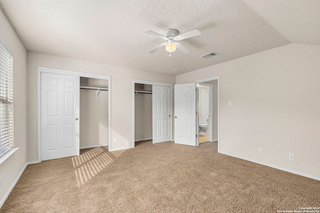 unfurnished bedroom featuring carpet floors, two closets, visible vents, vaulted ceiling, and a textured ceiling