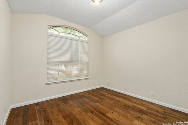 empty room featuring lofted ceiling, dark hardwood / wood-style floors, and a textured ceiling