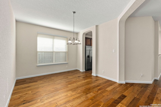 unfurnished dining area with hardwood / wood-style flooring, a notable chandelier, and a textured ceiling