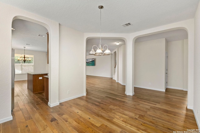 unfurnished dining area featuring hardwood / wood-style flooring, a notable chandelier, and a textured ceiling