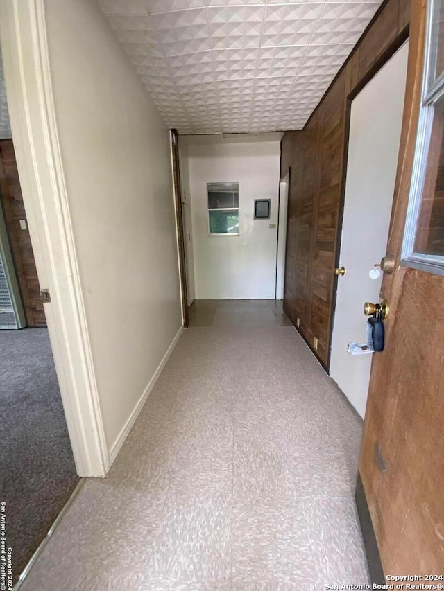 hallway featuring a paneled ceiling and wood walls