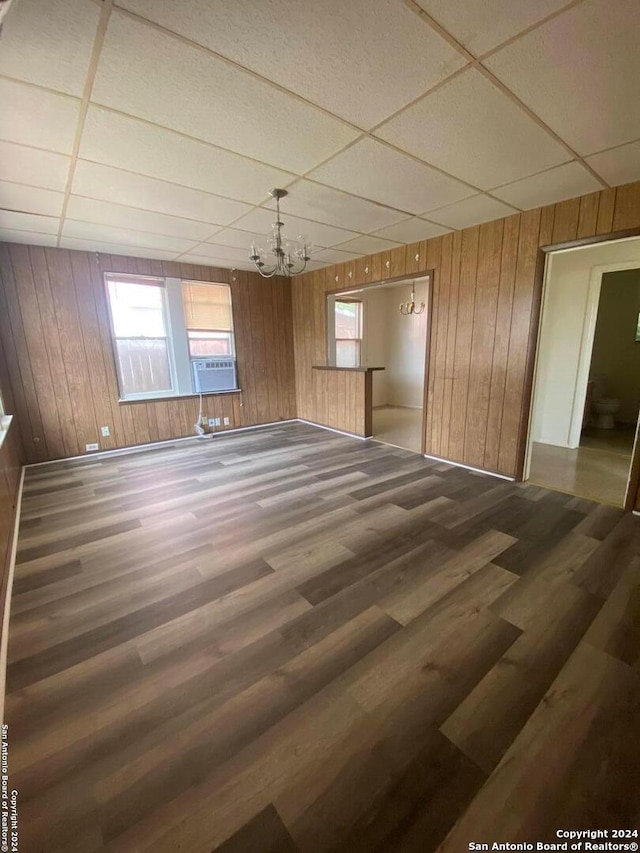 spare room featuring a paneled ceiling, wooden walls, and dark wood-type flooring