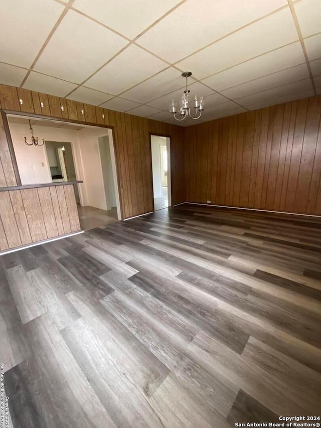 unfurnished living room featuring wooden walls, dark wood-type flooring, and a chandelier