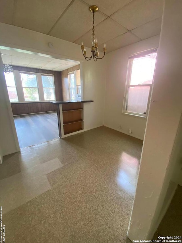 unfurnished dining area featuring a drop ceiling and an inviting chandelier