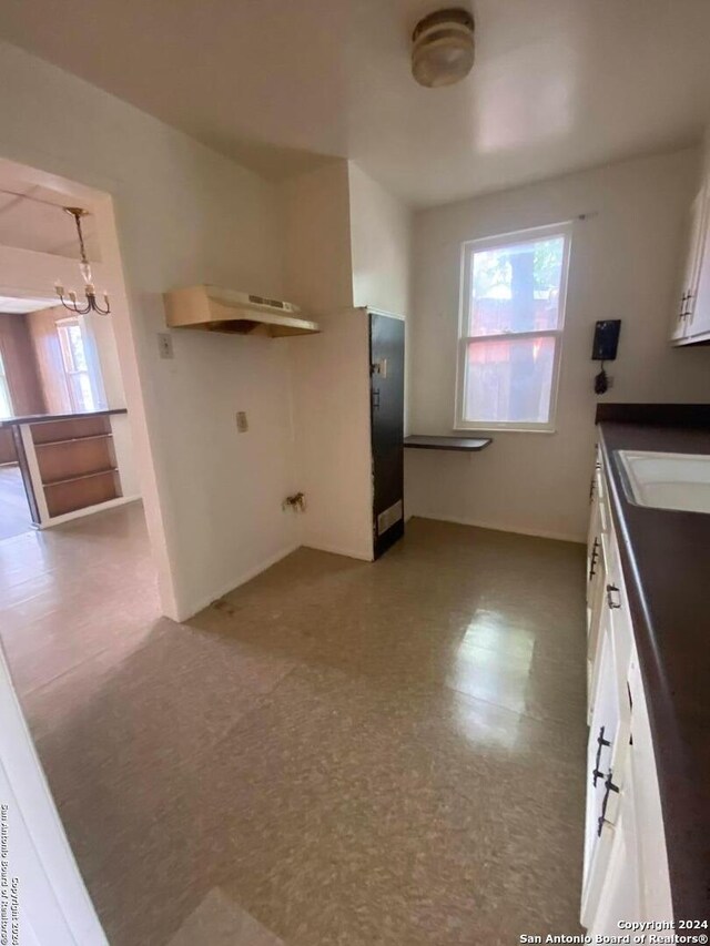 2019 Martin Luther King Dr, San Antonio, TX 78203 - kitchen with an inviting chandelier, a sink, dark countertops, under cabinet range hood, and white cabinetry