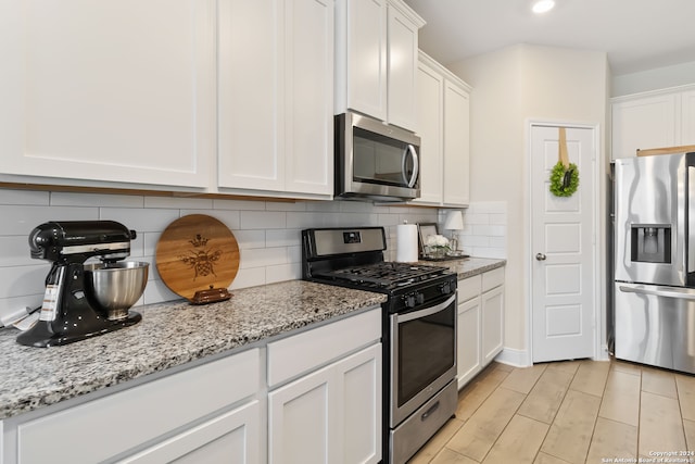 kitchen with light stone counters, decorative backsplash, white cabinetry, and stainless steel appliances