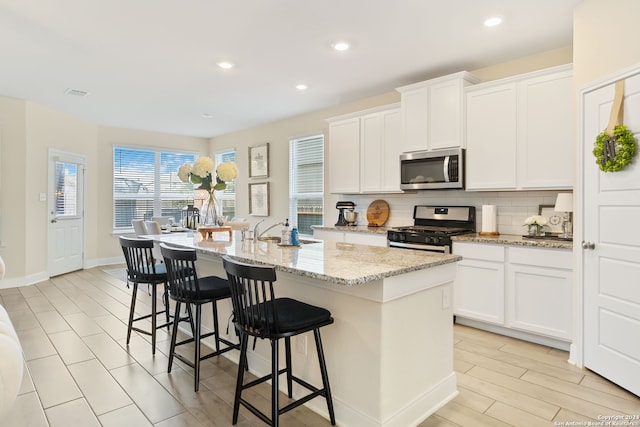 kitchen featuring a kitchen island with sink, appliances with stainless steel finishes, decorative backsplash, and white cabinetry