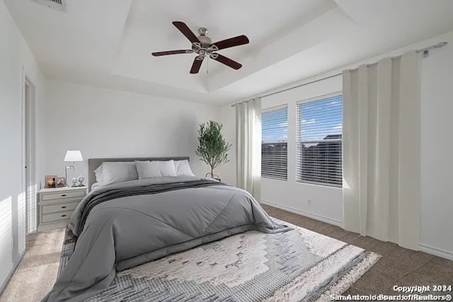 carpeted bedroom with ceiling fan and a raised ceiling