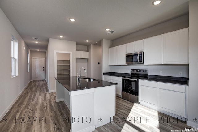 kitchen with appliances with stainless steel finishes, white cabinetry, hardwood / wood-style floors, a center island with sink, and sink