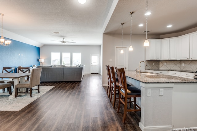 kitchen featuring dark stone counters, hanging light fixtures, a kitchen bar, and dark hardwood / wood-style floors