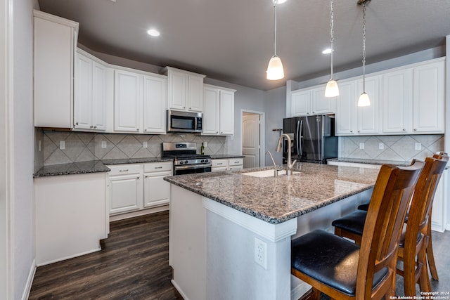 kitchen with pendant lighting, a center island with sink, white cabinetry, stainless steel appliances, and dark hardwood / wood-style floors