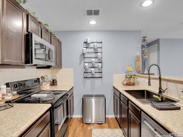 kitchen with light wood-type flooring, tasteful backsplash, sink, stainless steel appliances, and dark brown cabinetry