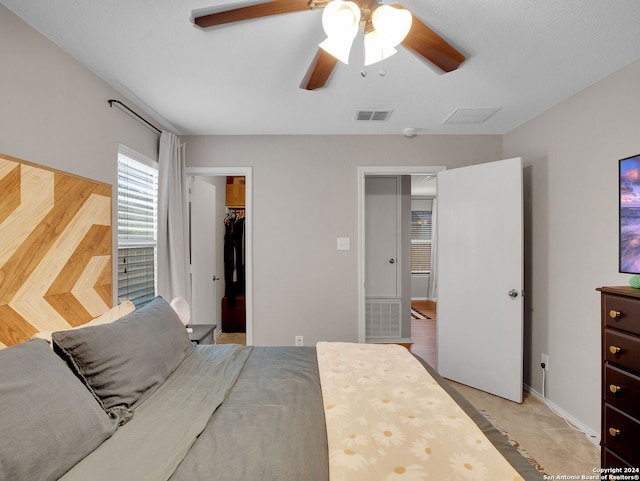 bedroom featuring ceiling fan, a closet, light carpet, and a walk in closet