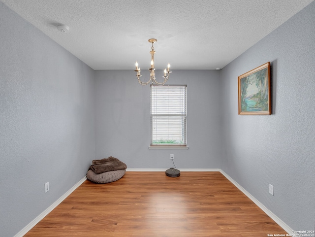 unfurnished room with a textured ceiling, wood-type flooring, and a notable chandelier