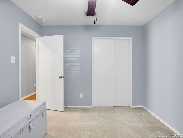 unfurnished bedroom with a textured ceiling, ceiling fan, light colored carpet, and a closet