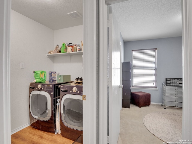 clothes washing area with a textured ceiling, washer and clothes dryer, and light wood-type flooring