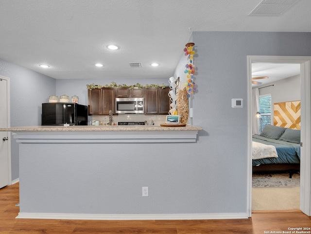 kitchen featuring light hardwood / wood-style floors, dark brown cabinets, black fridge, and kitchen peninsula