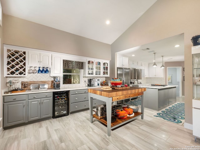 kitchen with pendant lighting, beverage cooler, stainless steel refrigerator, and white cabinetry