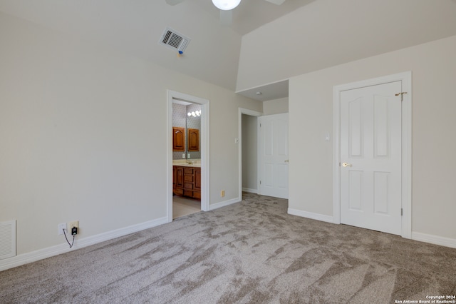 unfurnished bedroom with connected bathroom, vaulted ceiling, light carpet, and ceiling fan