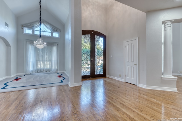 foyer entrance with a notable chandelier, high vaulted ceiling, decorative columns, light hardwood / wood-style flooring, and french doors