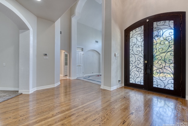 foyer entrance featuring french doors, light hardwood / wood-style floors, and a towering ceiling