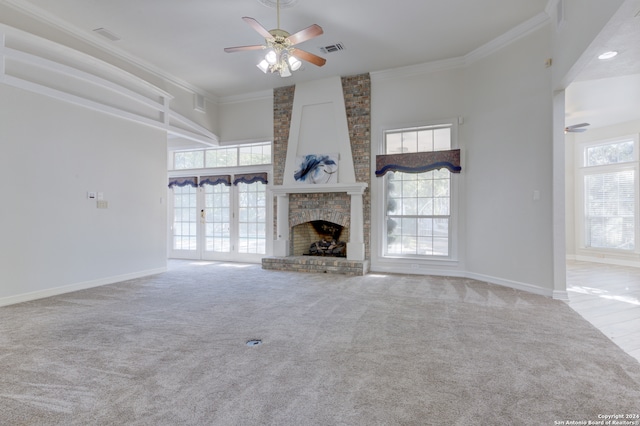 unfurnished living room featuring light carpet, ceiling fan, a brick fireplace, a high ceiling, and crown molding