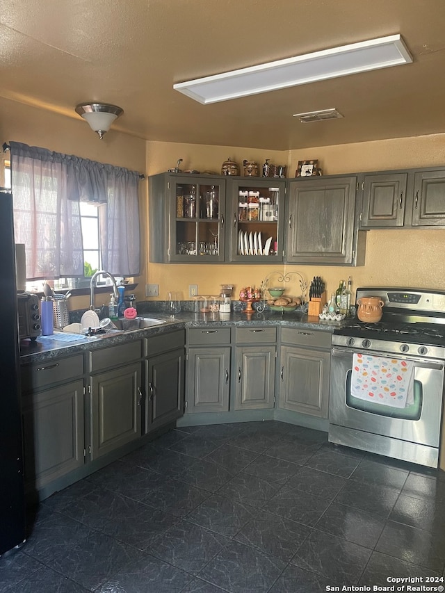 kitchen featuring black fridge, gray cabinets, stainless steel gas range, and sink