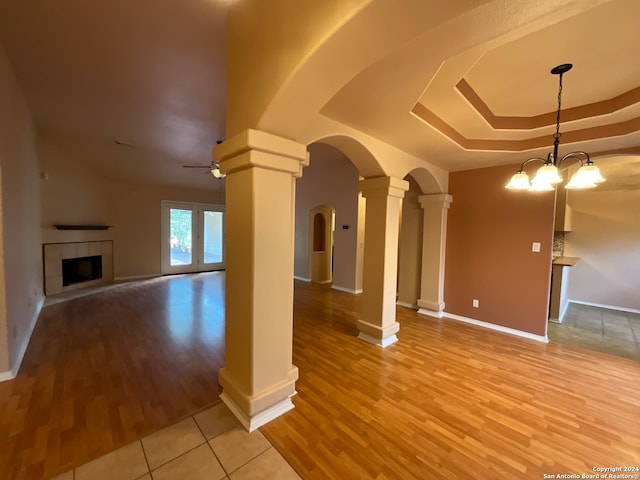 unfurnished living room featuring a fireplace, a tray ceiling, light hardwood / wood-style floors, and ornate columns