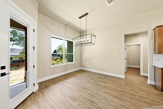 unfurnished dining area with light wood-type flooring, a chandelier, and a healthy amount of sunlight