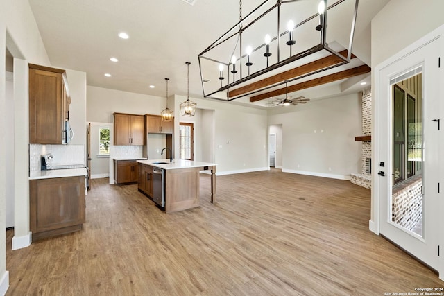 kitchen with decorative backsplash, an island with sink, beamed ceiling, light wood-type flooring, and decorative light fixtures