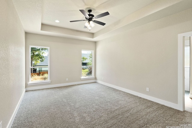 carpeted spare room featuring a raised ceiling and ceiling fan