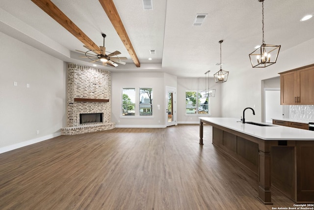 kitchen featuring pendant lighting, sink, a center island with sink, dark wood-type flooring, and a fireplace