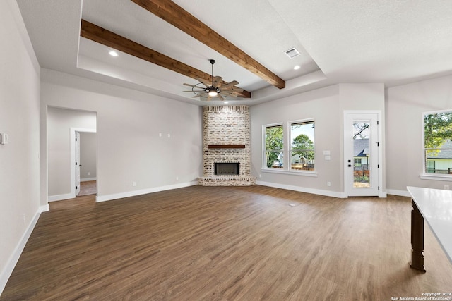 unfurnished living room with a brick fireplace, beam ceiling, dark wood-type flooring, and ceiling fan