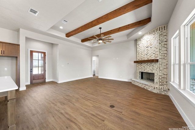 unfurnished living room featuring a fireplace, beam ceiling, dark hardwood / wood-style flooring, and ceiling fan