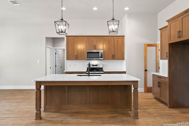 kitchen featuring pendant lighting, stainless steel appliances, a center island with sink, and light wood-type flooring