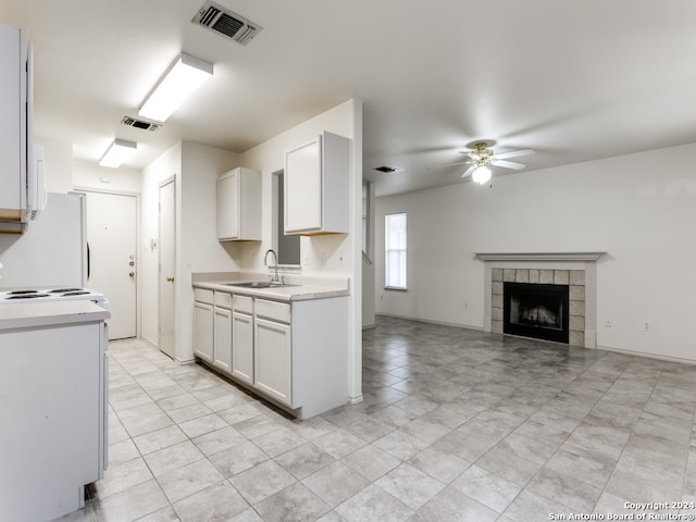 kitchen with ceiling fan, sink, a tiled fireplace, white cabinetry, and white fridge