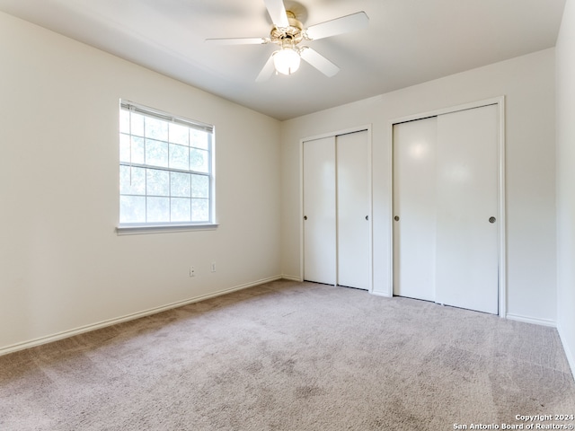 unfurnished bedroom featuring ceiling fan, multiple closets, and light carpet