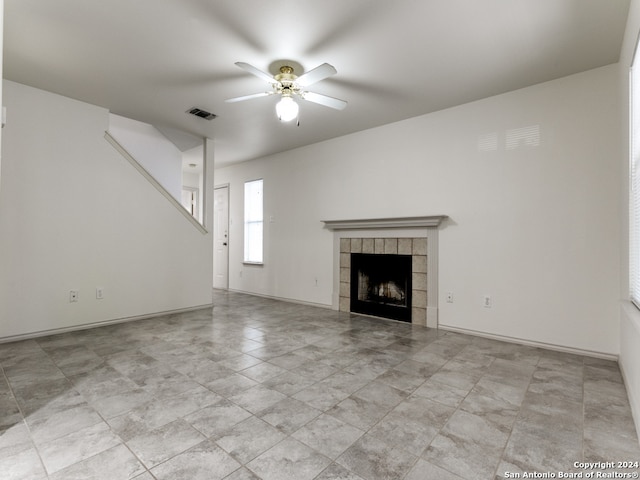 unfurnished living room with a tiled fireplace and ceiling fan