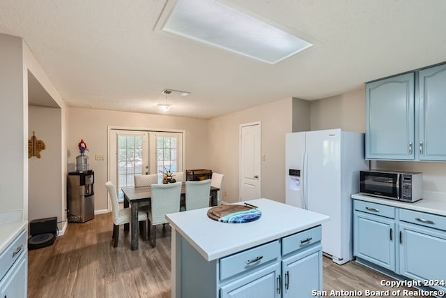 kitchen with blue cabinets, french doors, hardwood / wood-style flooring, a center island, and white fridge with ice dispenser